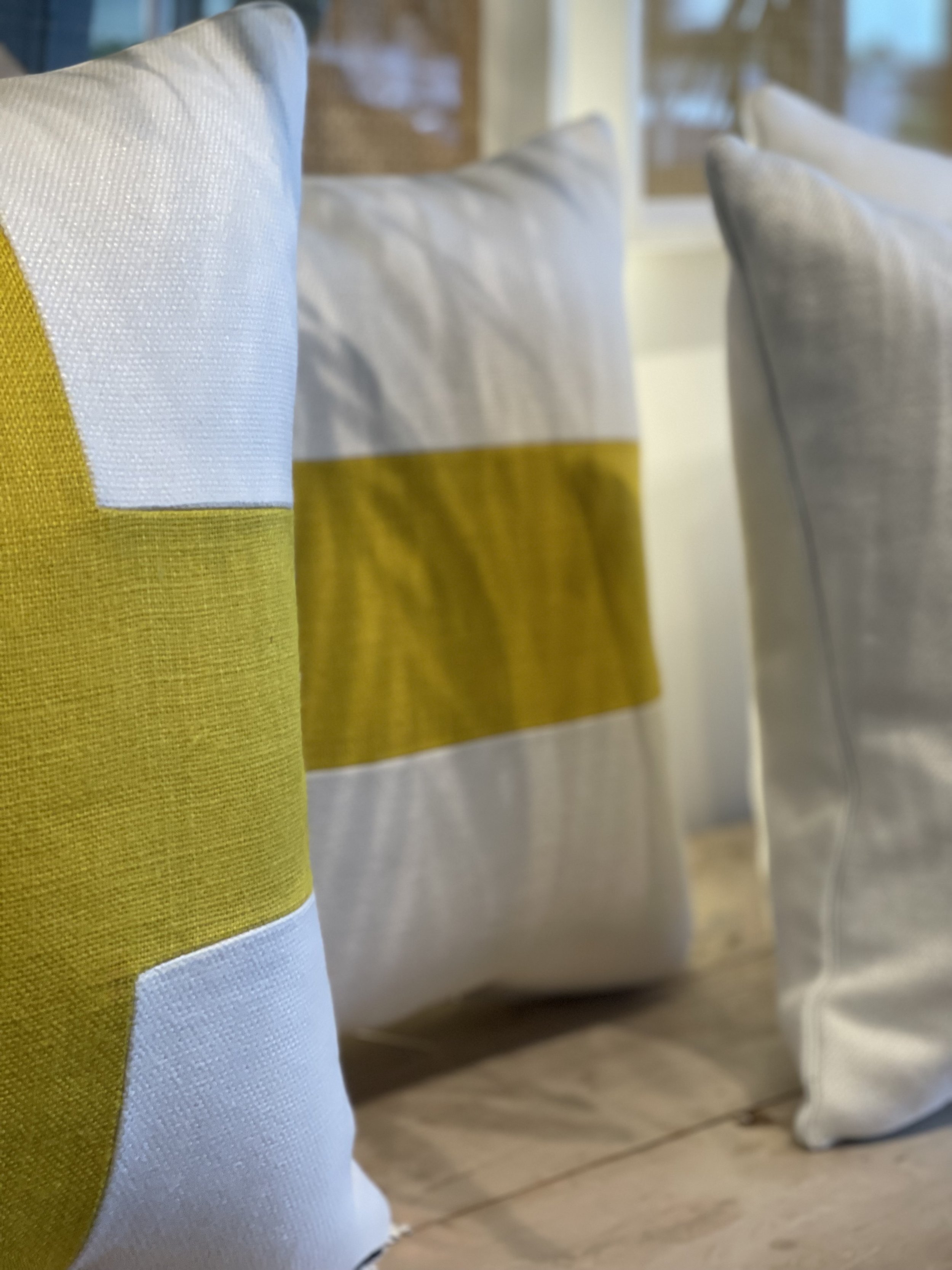 Close-up of a yellow and white striped fabric, possibly a cushion or pillow, with other cushions in the background.