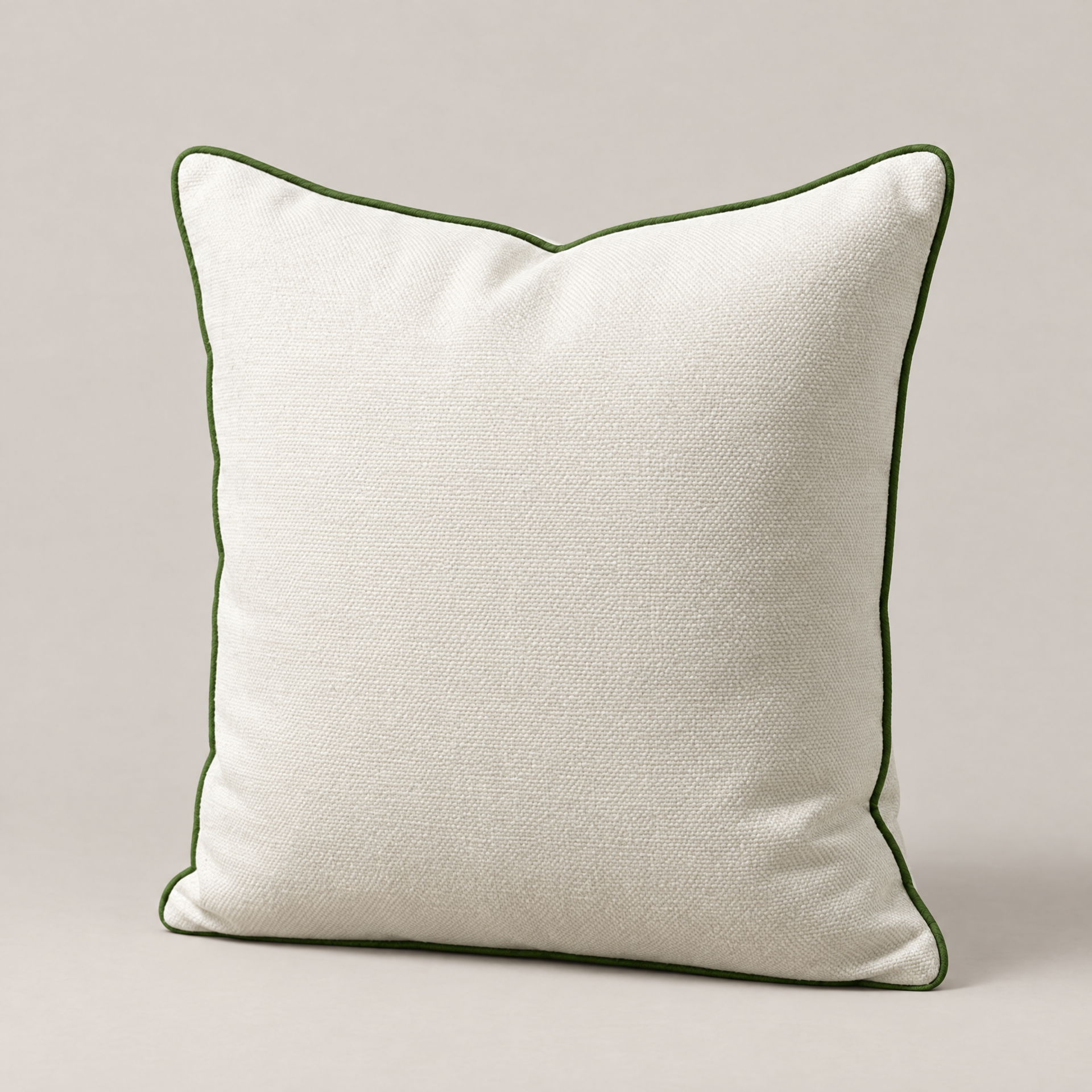 An ivory linen Verdado pillow with green piping resting on a surface.