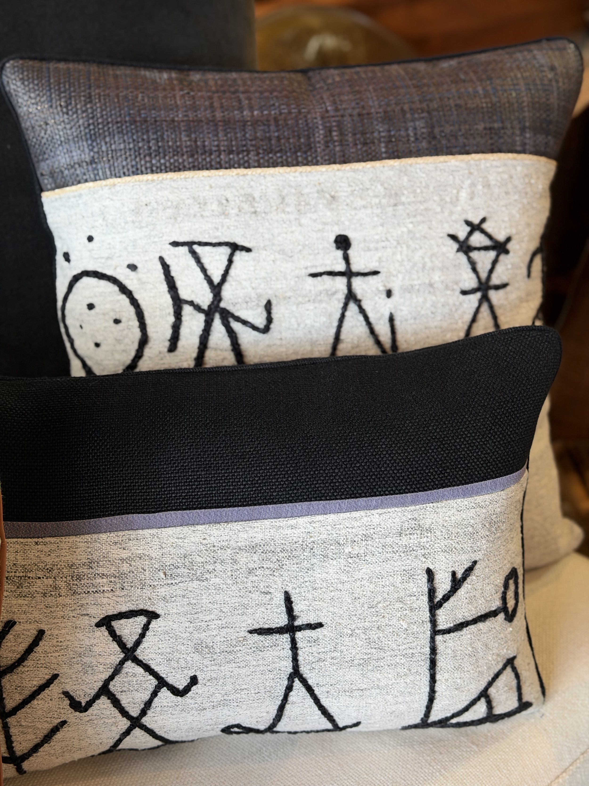 A Anatolian rug pillow with  black embroidered mathematical symbols and formulas, with black linen top section of the pillow.  Palme x Patrick Sutton Pillow Collection.