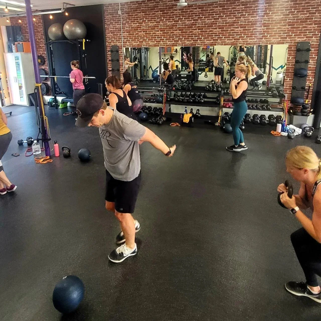 People exercising in a gym with brick walls, mirrors, and various workout equipment.