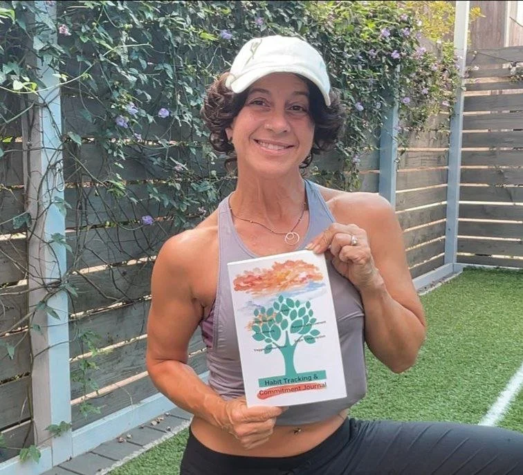 A woman smiling outdoors, wearing a white cap and athletic tank top, holding a paper with a tree illustration and the words 'Habit Tracking & Commitment Journal.' She stands next to a wooden fence and greenery.