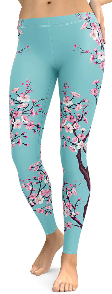 A close-up of a woman's lower body wearing light blue leggings with a cherry blossom branch pattern.
