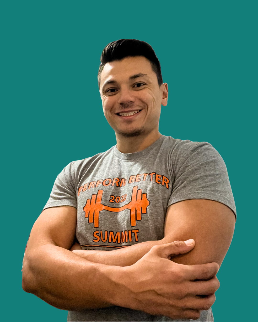 A smiling young man with short dark hair in a gray T-shirt with orange text and graphic, standing against a teal background with his arms crossed.