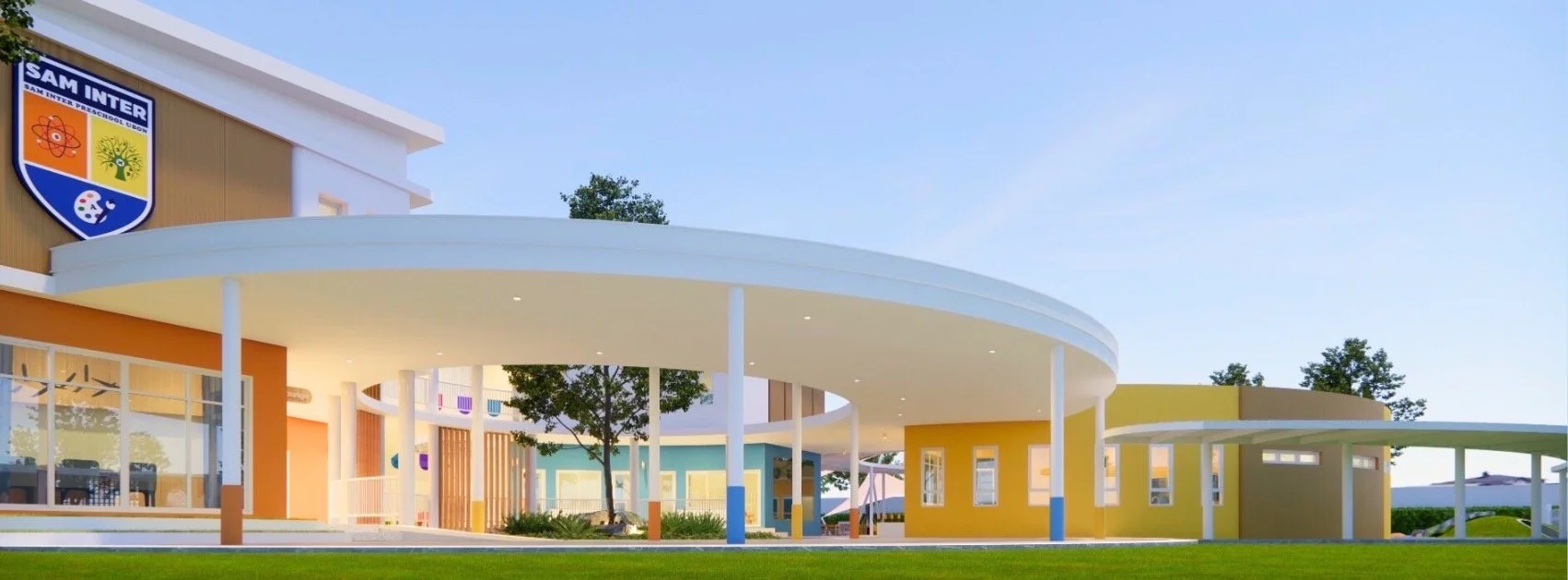 A modern building with a curved white roof, colorful walls in orange, yellow, and blue, and large windows. The scene includes a green lawn, trees, and a clear sky.