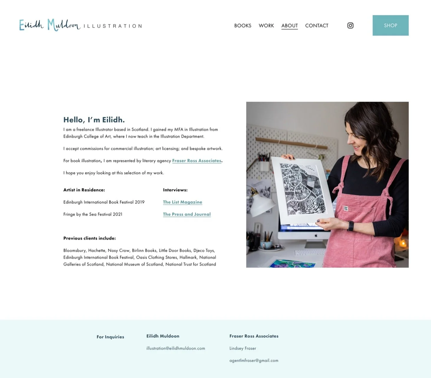 A woman in a pink apron holding an art print in a bright, organized workspace.