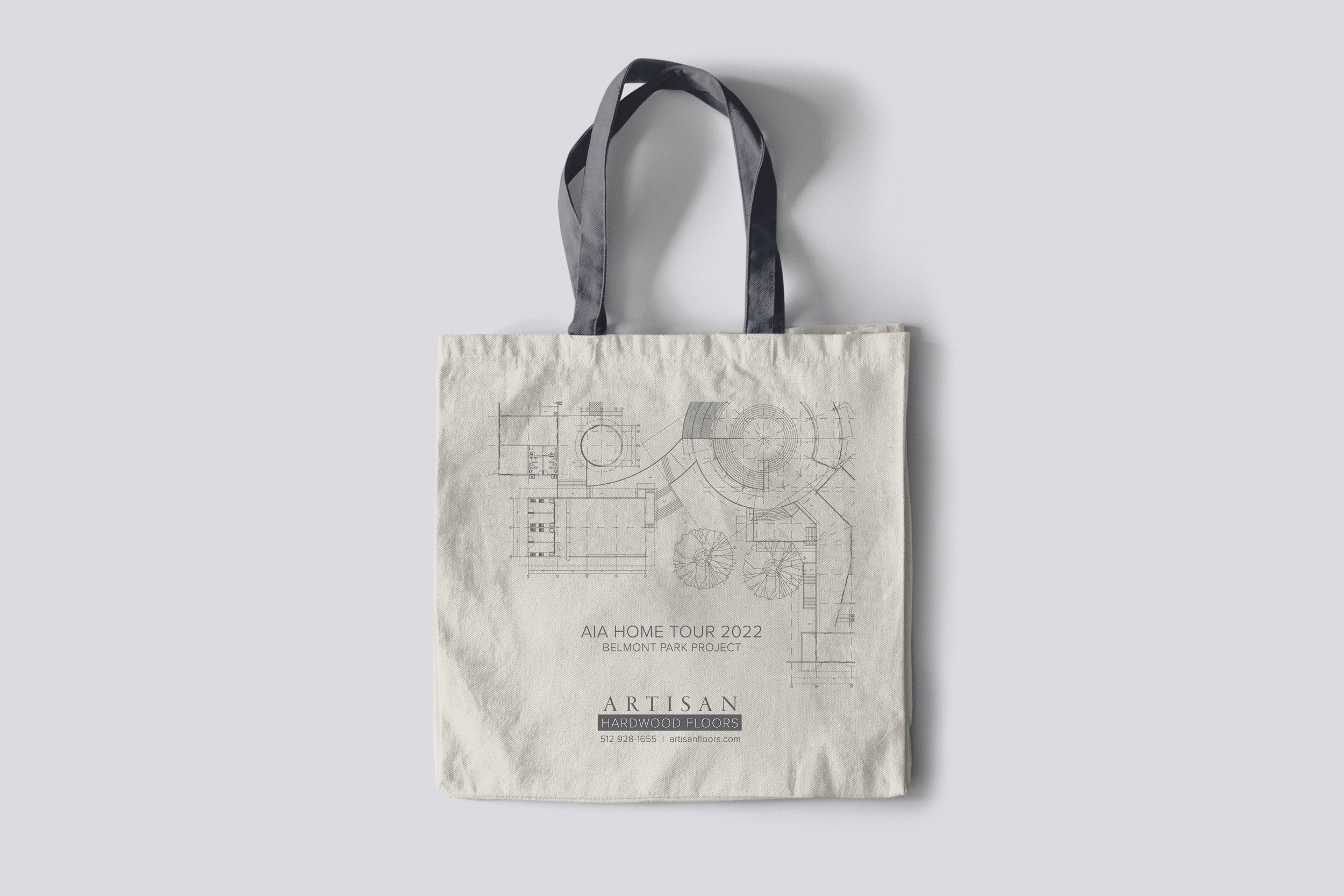 A beige tote bag with black and gray handles featuring a detailed architectural blueprint design and text about a home tour and flooring company.