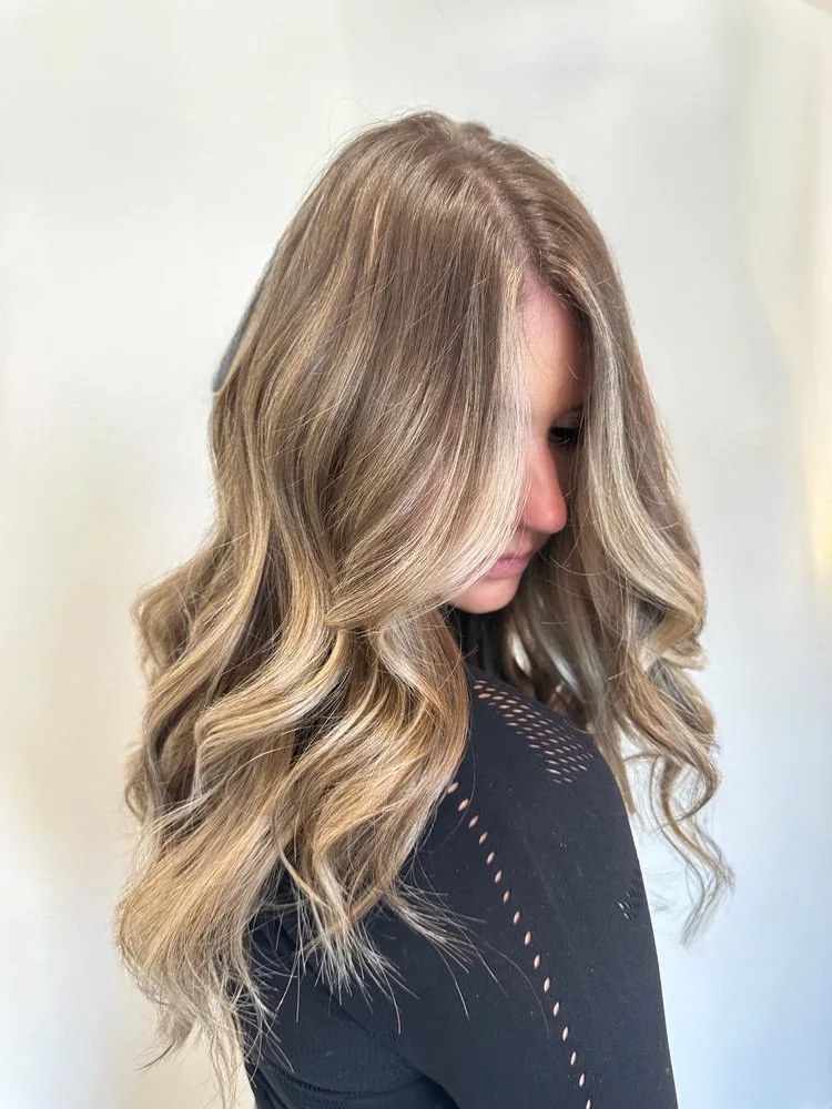 Long blonde waves with darker roots and soft dimension.