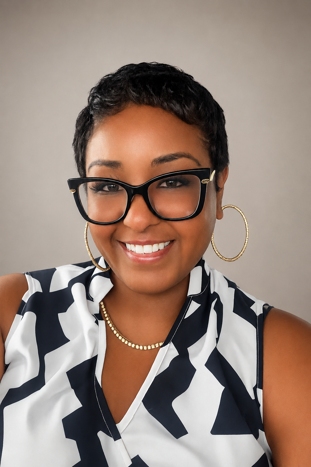 Portrait of a smiling woman with short dark hair, wearing large black glasses, gold hoop earrings, a gold necklace, and a black and white patterned sleeveless top.