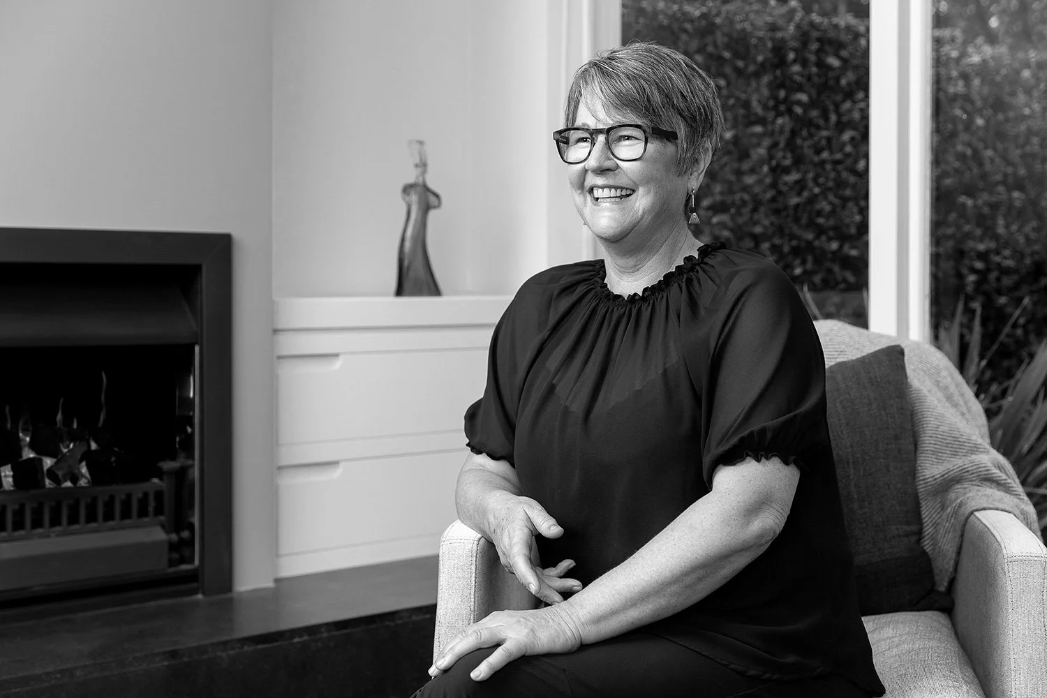 Clinical Psychologist and Paediatric Neuropsychologist, Megan Fowler smiling and sitting on a chair in a living room with a fireplace.