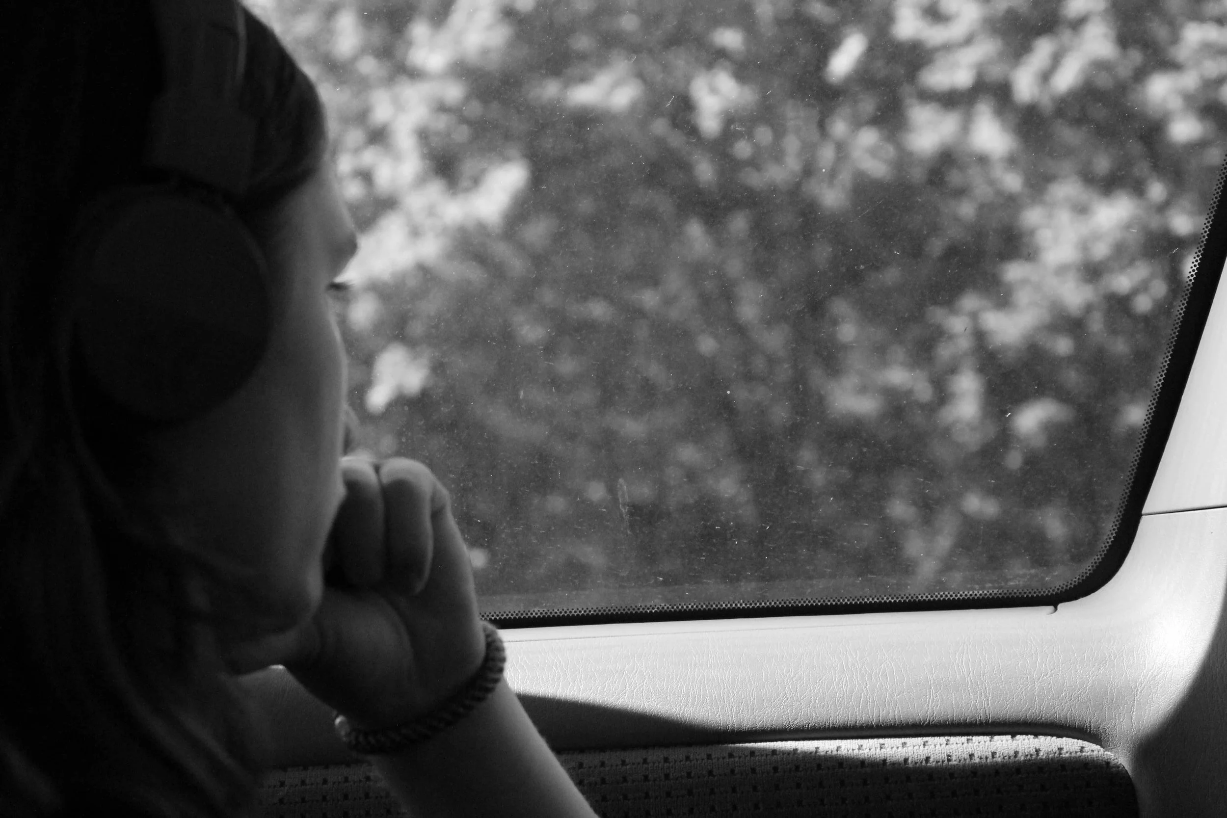 black and white photo of a woman gazing out of a car window, hand on her chin