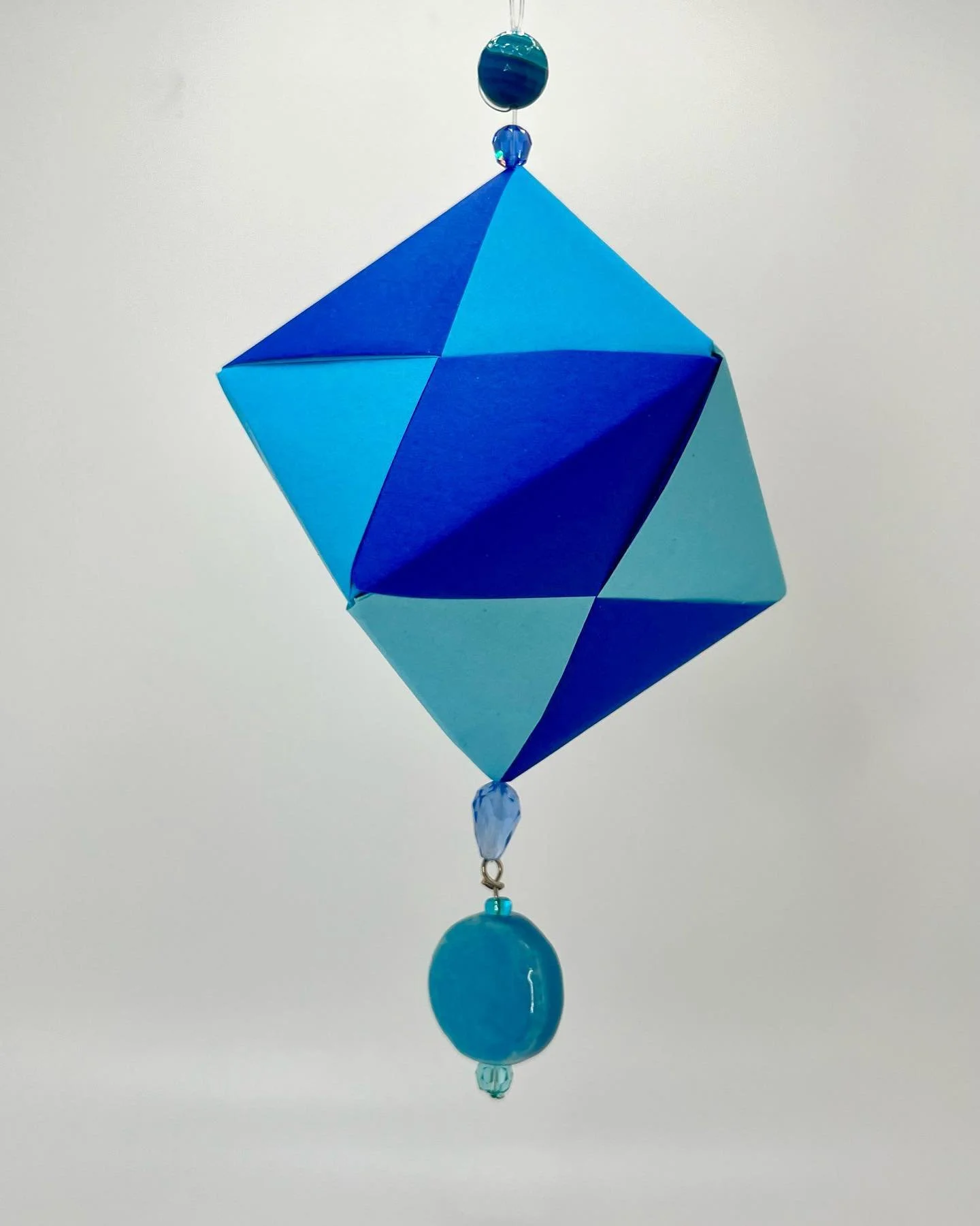 A blue cube with a handmade bead pendant 💙🩵 
link in bio for my shop ✨

#origami #smallbusiness #papercraft #handmade