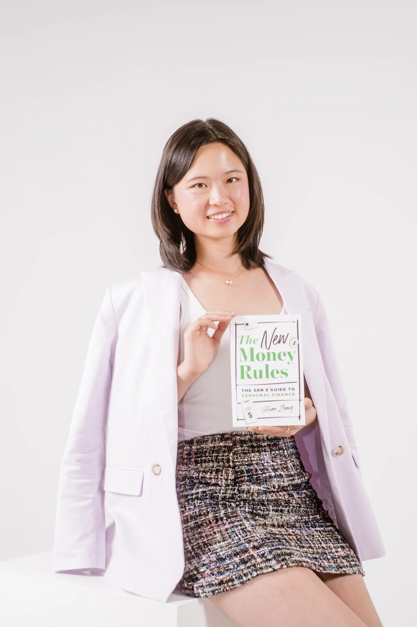 Lillian Zhang, an Asian American author, holds the book The New Money Rules: The Gen Z Guide to Personal Finance