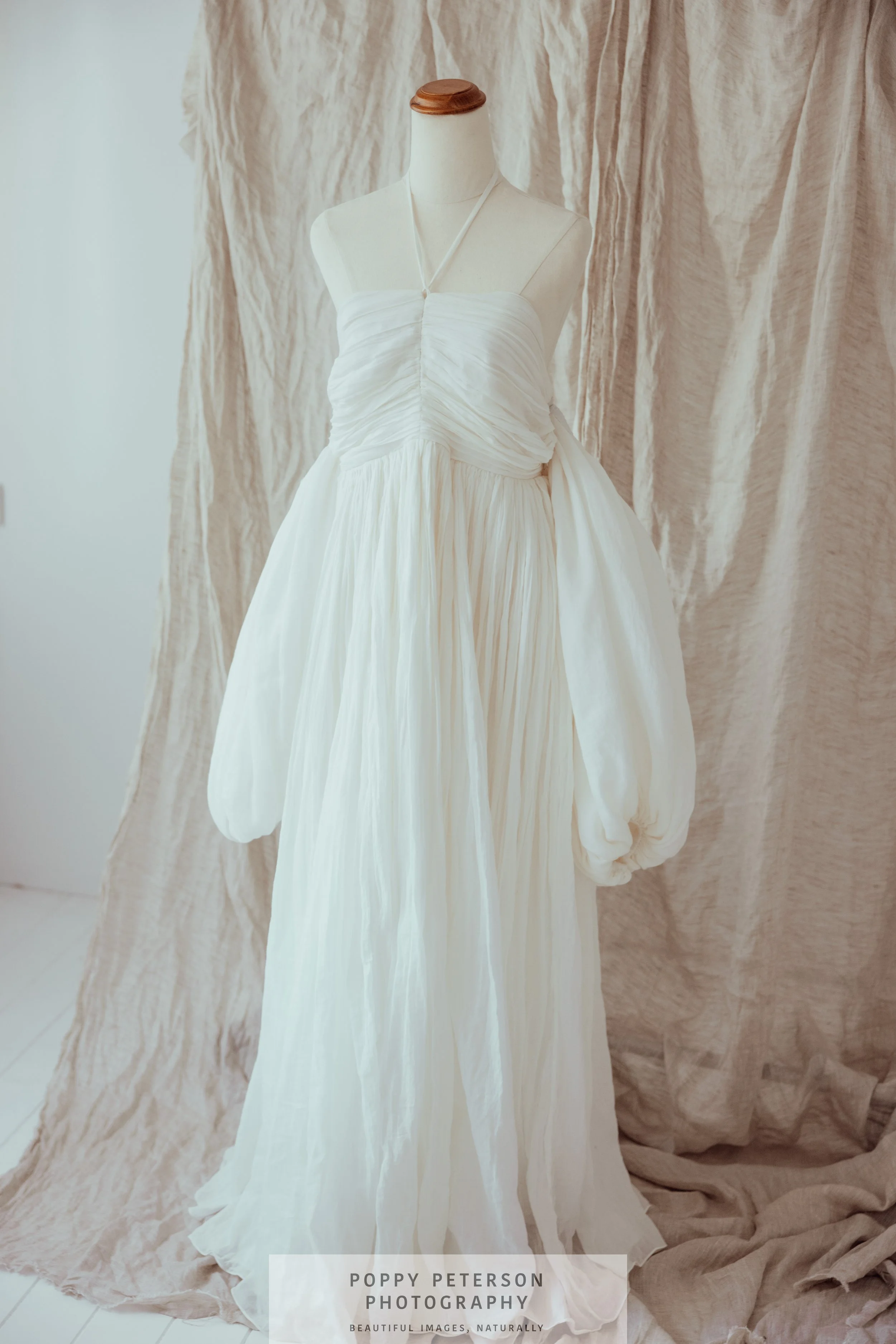 A white, strapless gown displayed on a dress form, with a ruched bodice and full, flowing skirt. Rooh Design Collective,maternity gowns, spell, co + ry, Fillyboo, Jen's Pirate Booty, Bird and Kite, Hazel and Folk, bridal, breast feeding friendly