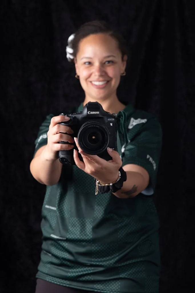 Woman smiling, holding Canon camera in front of her, dark background
