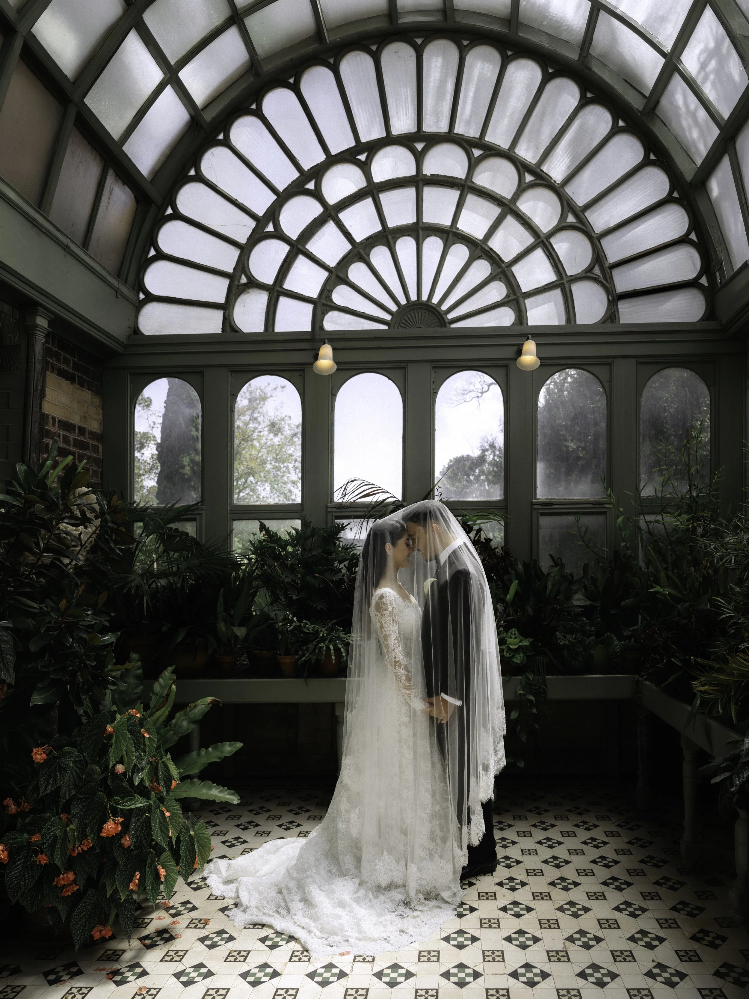 A man and woman holding hands in an art gallery, the woman raising her hand with her palm facing outward, and paintings hanging on red walls in the background.