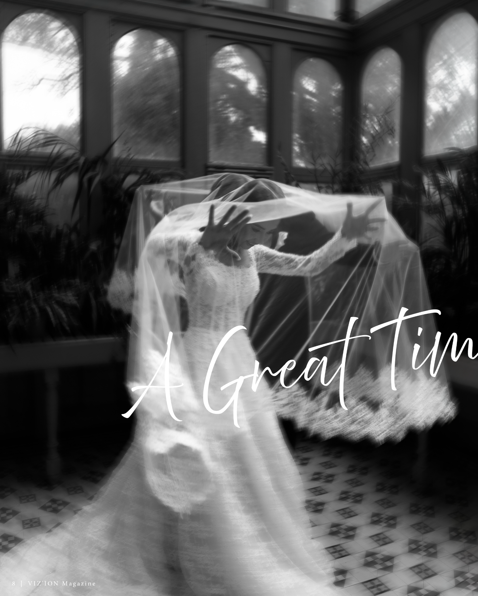 Black and white photo of a woman dressed in a wedding gown, standing inside an enclosed porch with large windows. The woman is smiling, touching her forehead with one hand and holding her veil with the other. The background shows trees outside the windows.
