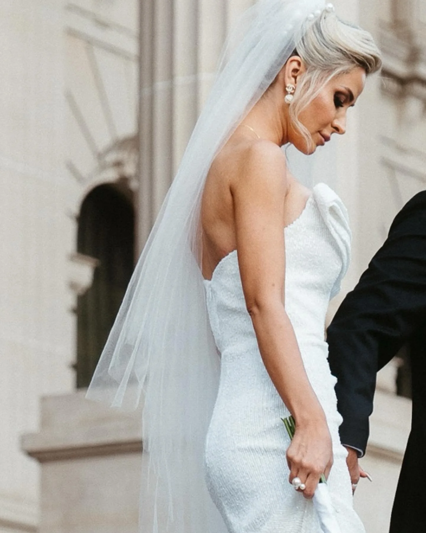 A bride in a white wedding dress and veil holding a bouquet, standing next to an officiant during a wedding ceremony.