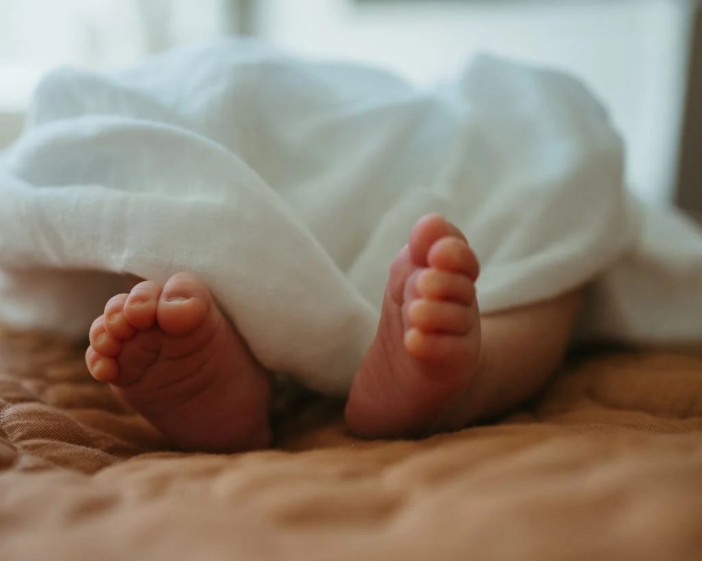 Close-up of a baby's tiny feet on a brown surface, partially covered by a white cloth.