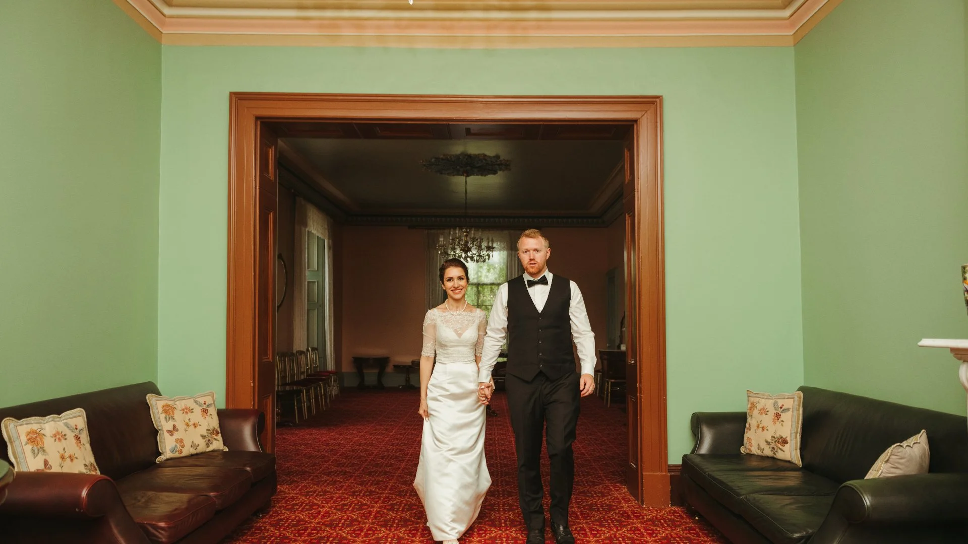 Bride and groom walking hand in hand through a decorated room during their wedding celebration.