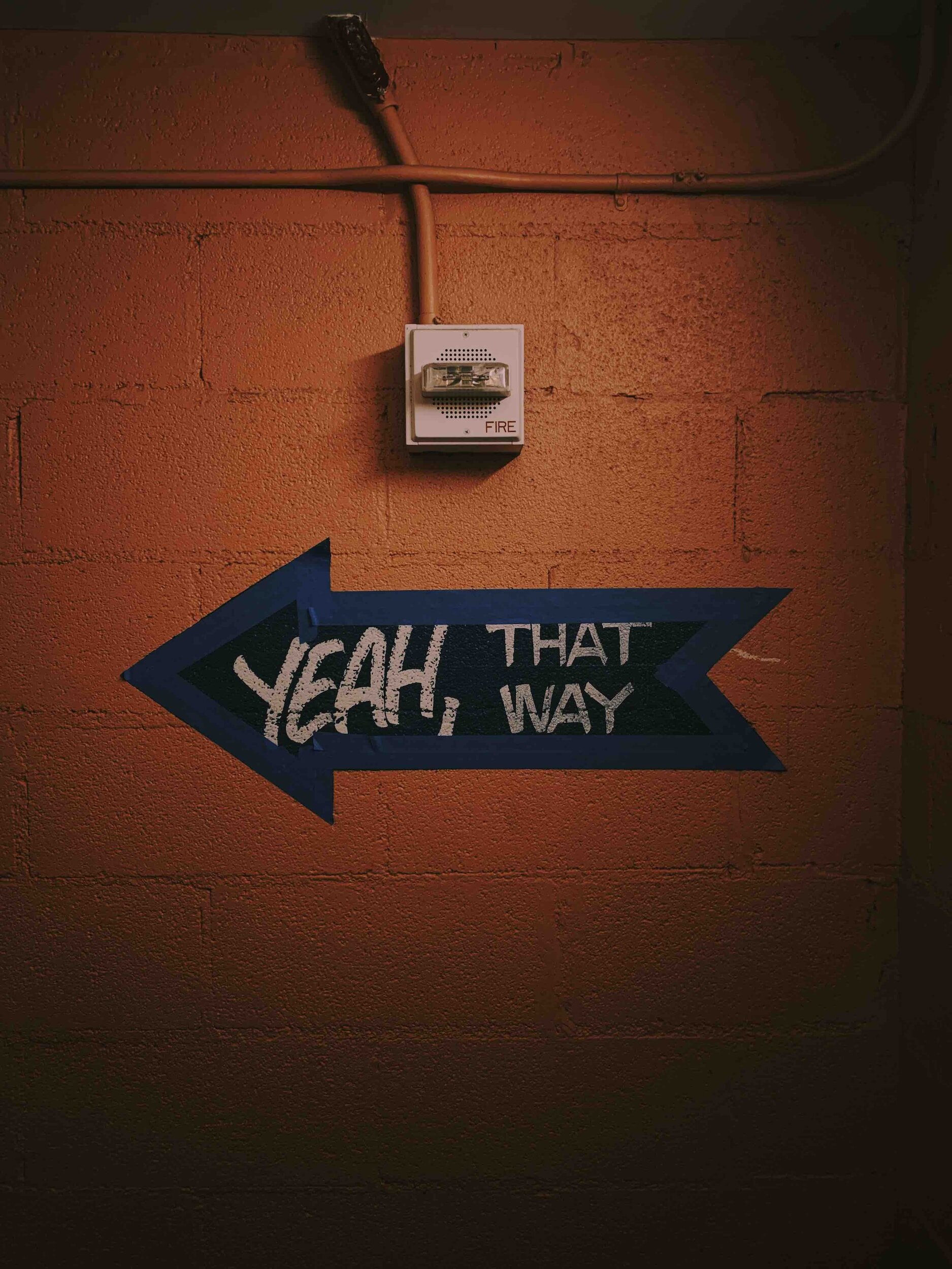 A blue arrow sign on an orange brick wall points to the left with the words "YEAH THAT WAY" written on it.