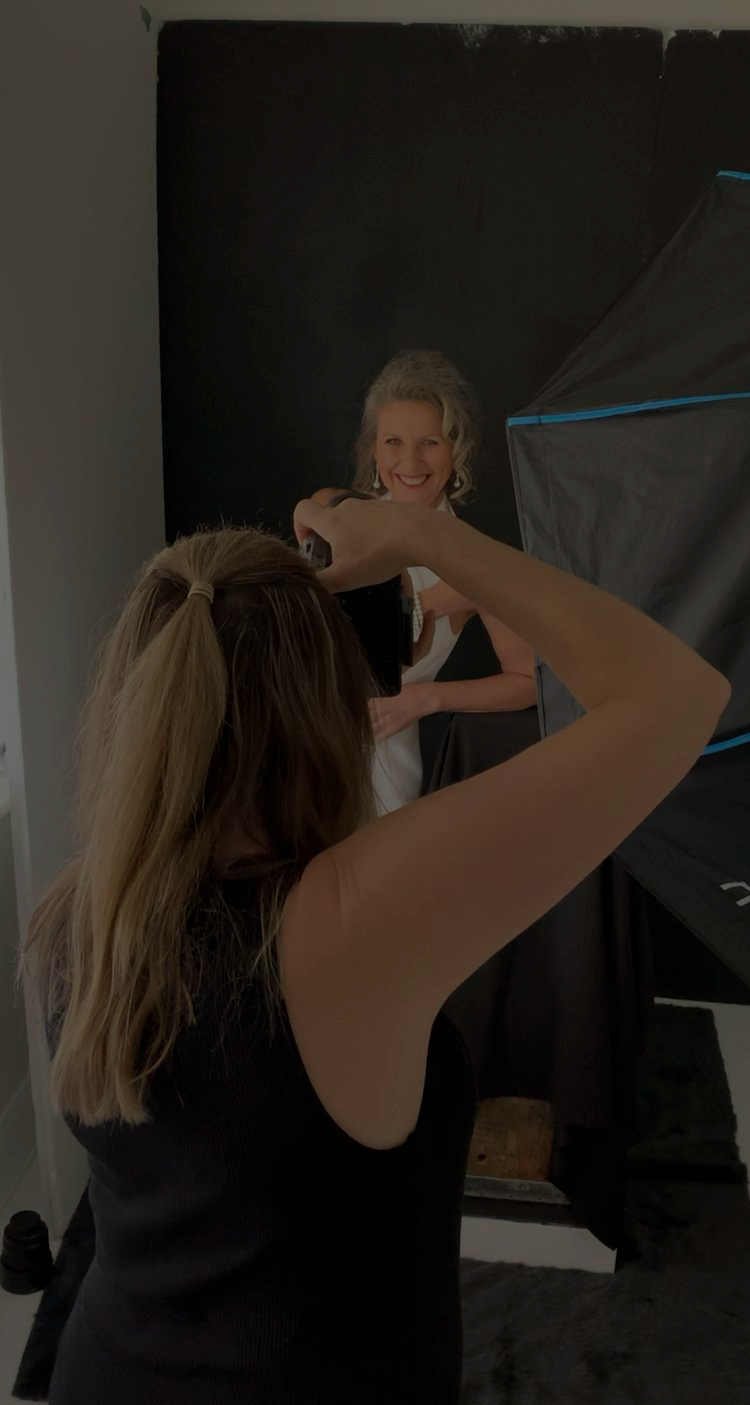 A woman photographing a smiling model in a photography studio with dark lighting and backdrop.