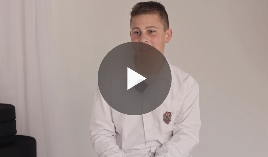 A teenage boy in a white shirt sits in front of a plain background.