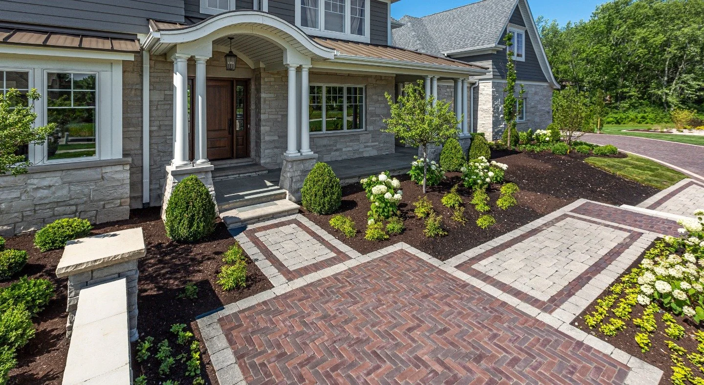 Gorgeous paver walkway in front of rich stone home with mulching and garden