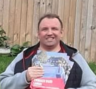 Man holding a sign outdoors with wooden fence in the background