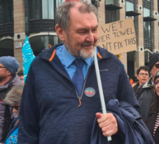 A man with gray hair and a beard holding a sign at a protest or rally