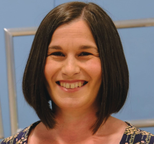 A woman with shoulder-length dark hair smiling in front of a blue background and a metal frame.
