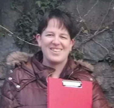 Woman outdoors holding a red clipboard, smiling