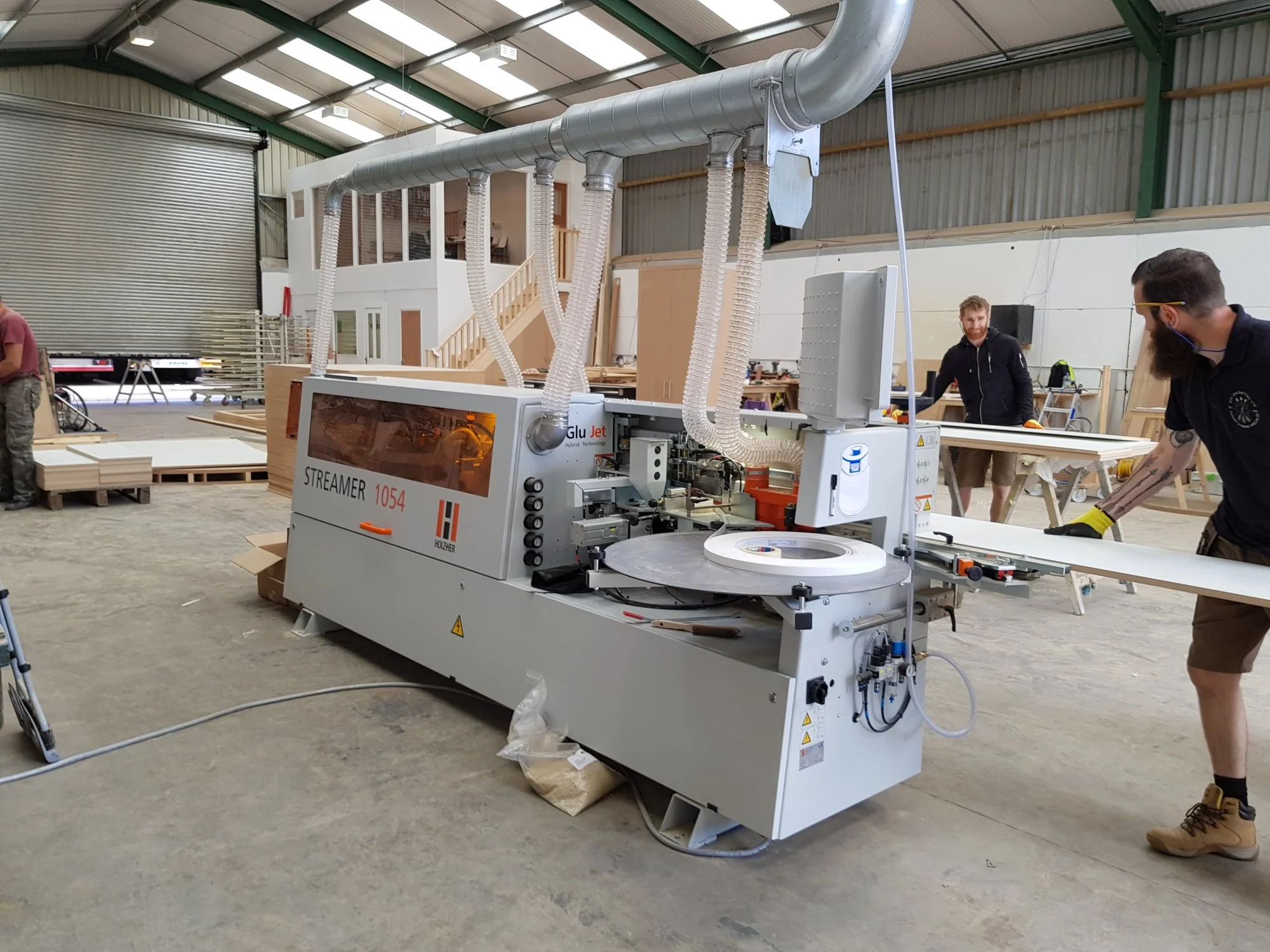 Industrial woodworking workshop with a CNC machine labeled 'STREAMER 1054' and workers operating and inspecting the equipment.