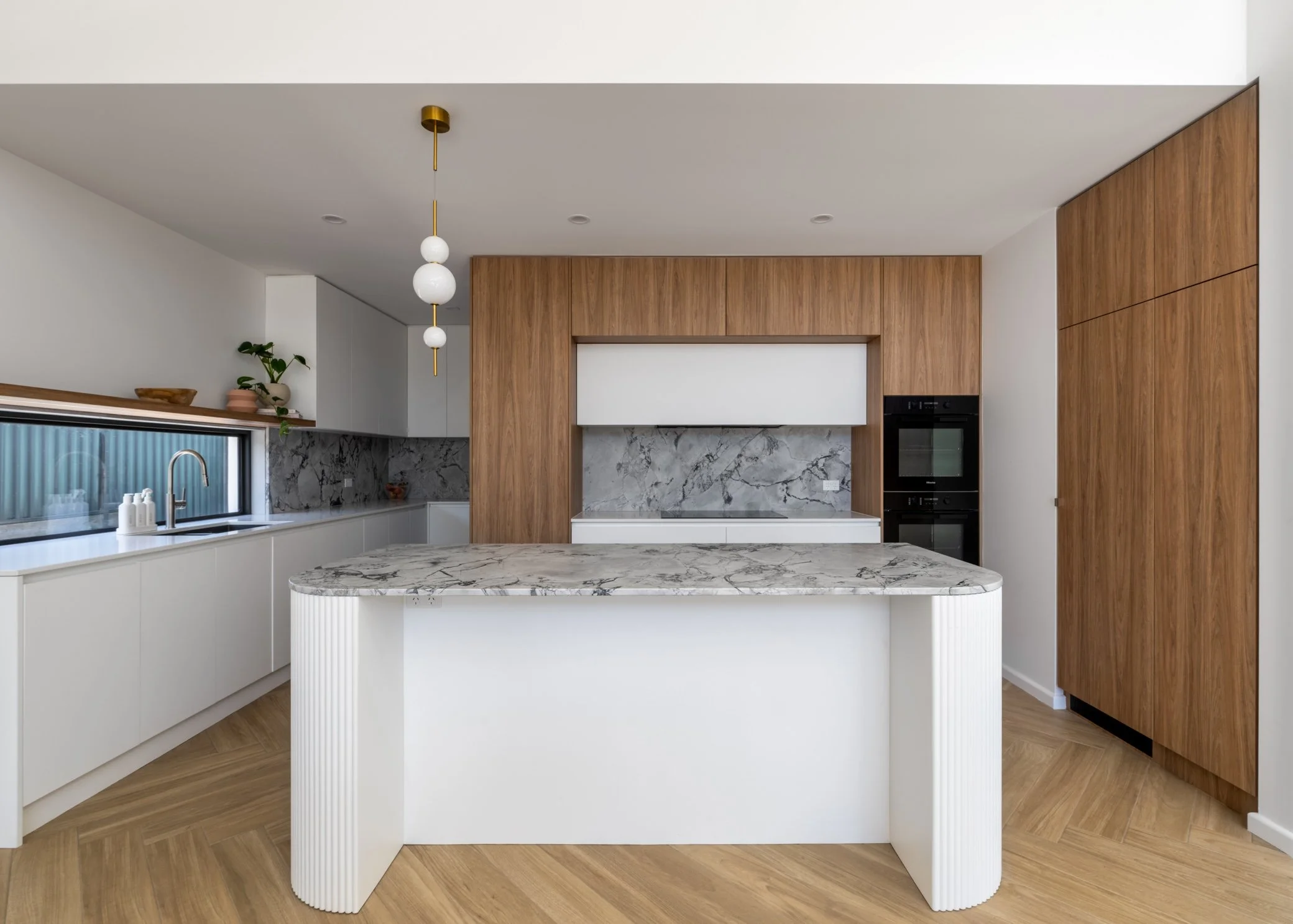 Modern kitchen with white cabinets, marble countertops, a central island, wooden accents, and built-in appliances.