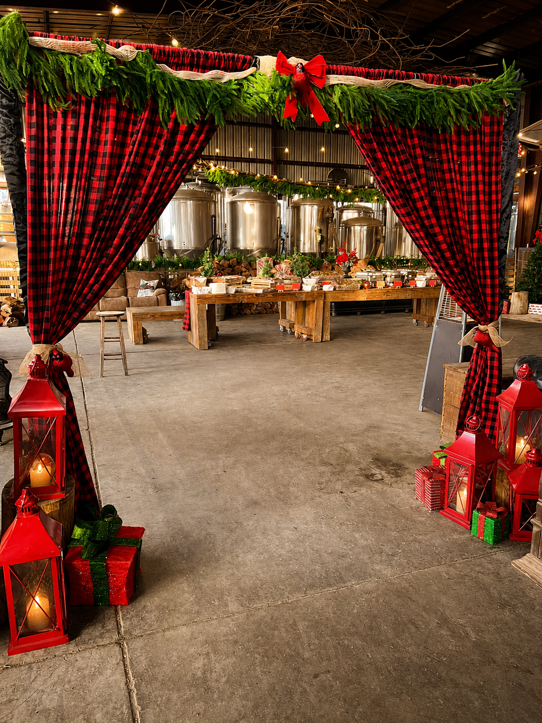 A festive holiday entrance framed with red-and-black buffalo plaid draping, lush evergreen garland, red lanterns, and wrapped gifts, creating a warm and inviting arrival experience for guests.