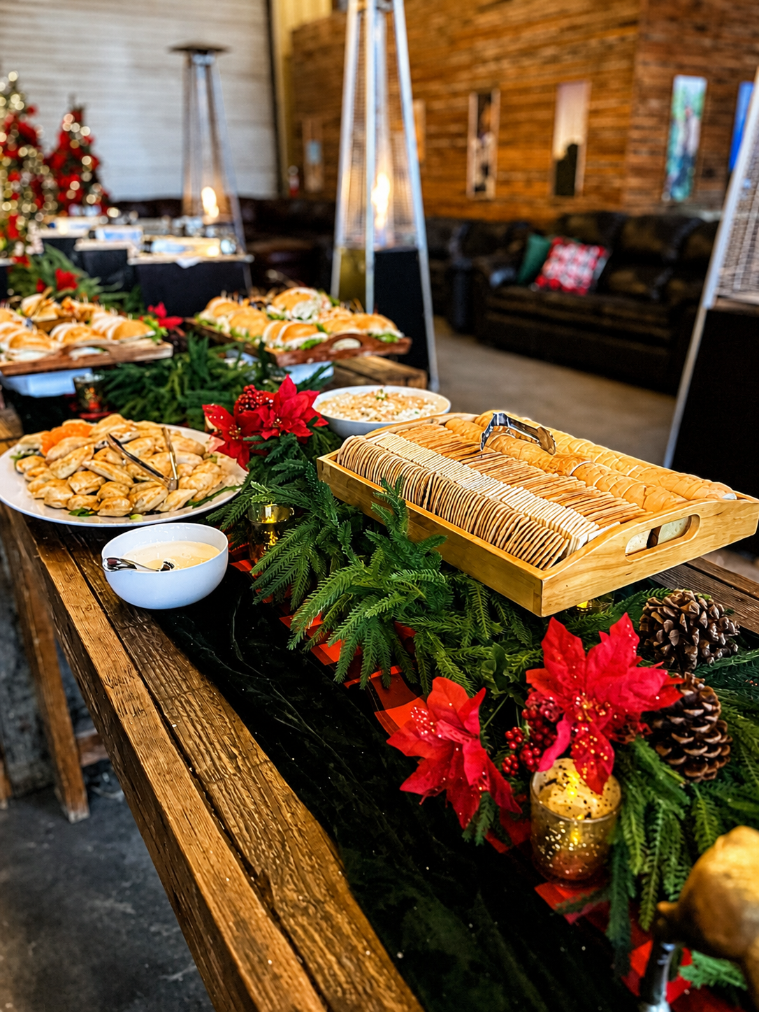 Holiday catering display with golden appetizers, sandwiches, evergreen garland and seasonal table décor.