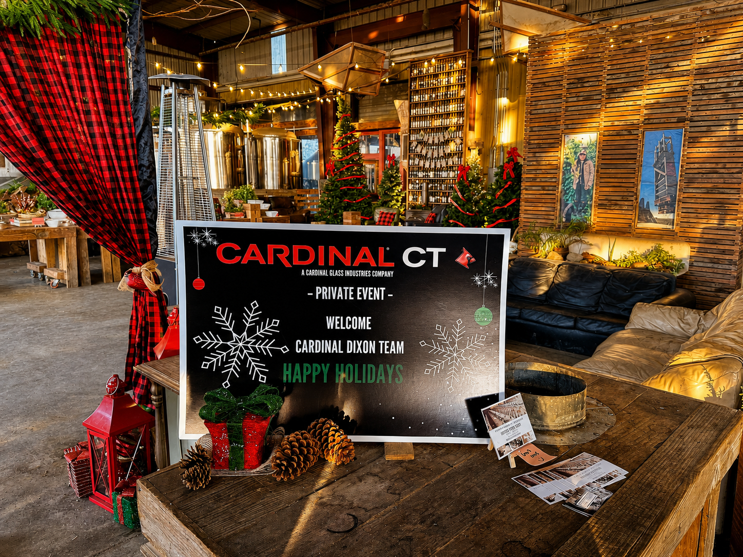 A customized corporate event welcome area featuring branded signage, holiday décor, pinecones, lanterns, and rustic accents designed to create a polished guest arrival experience.