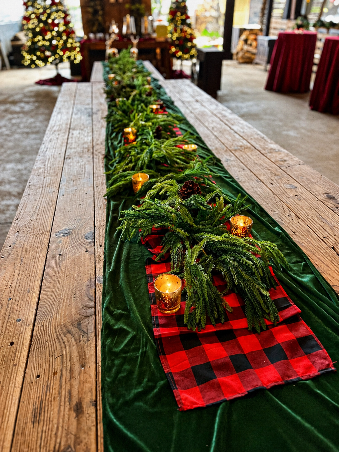 Rustic holiday table centerpiece with evergreen branches, buffalo plaid accents, pinecones and gold votive candles.