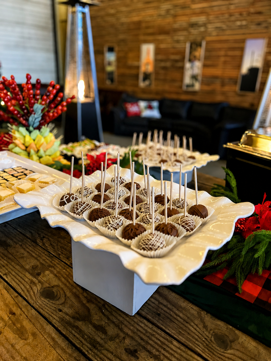 Holiday dessert table featuring chocolate treats, festive greenery, red accents and elegant white serving platters.