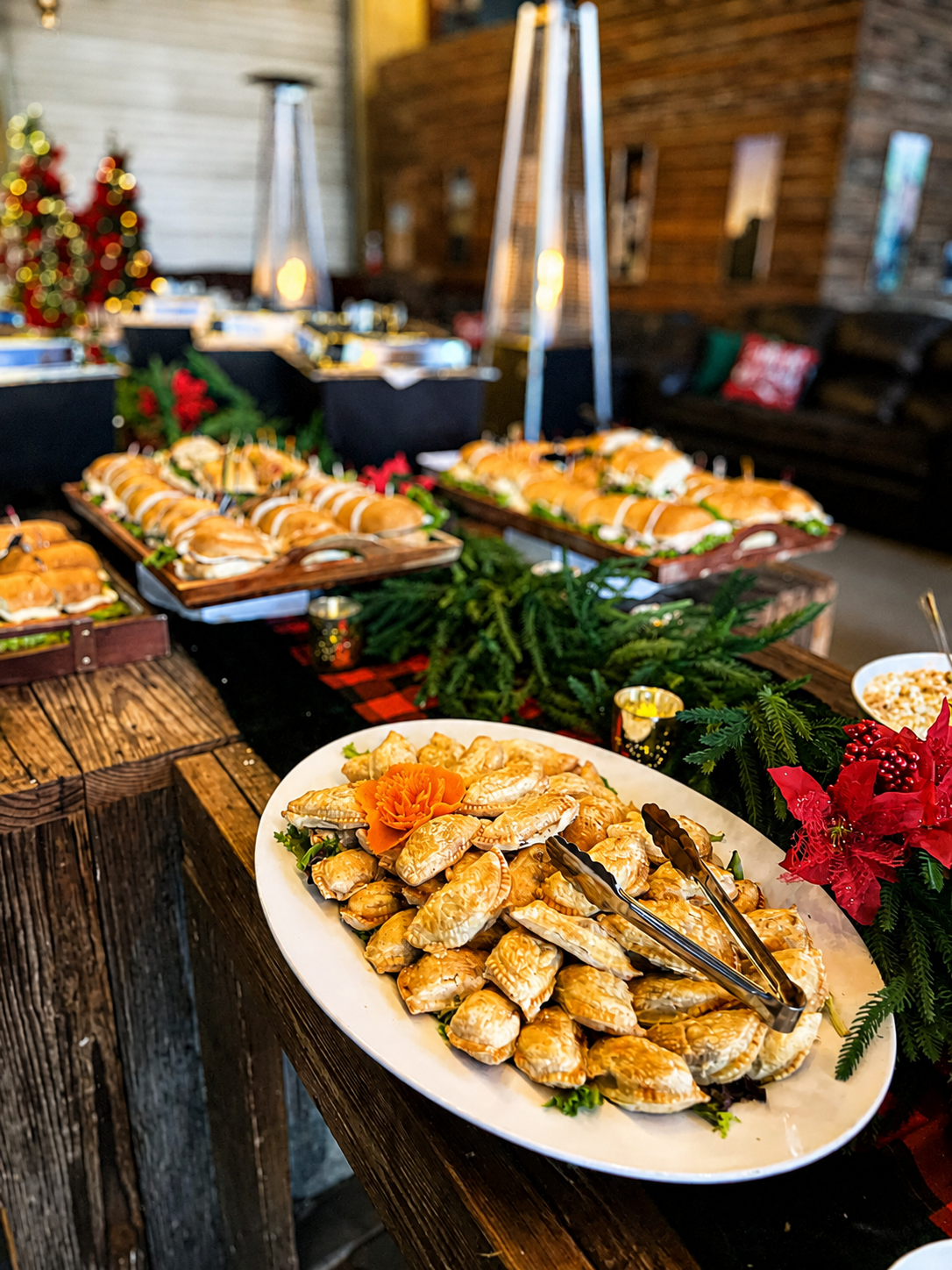 Holiday party buffet table styled with evergreen garland, red poinsettias, crackers and festive serving displays.