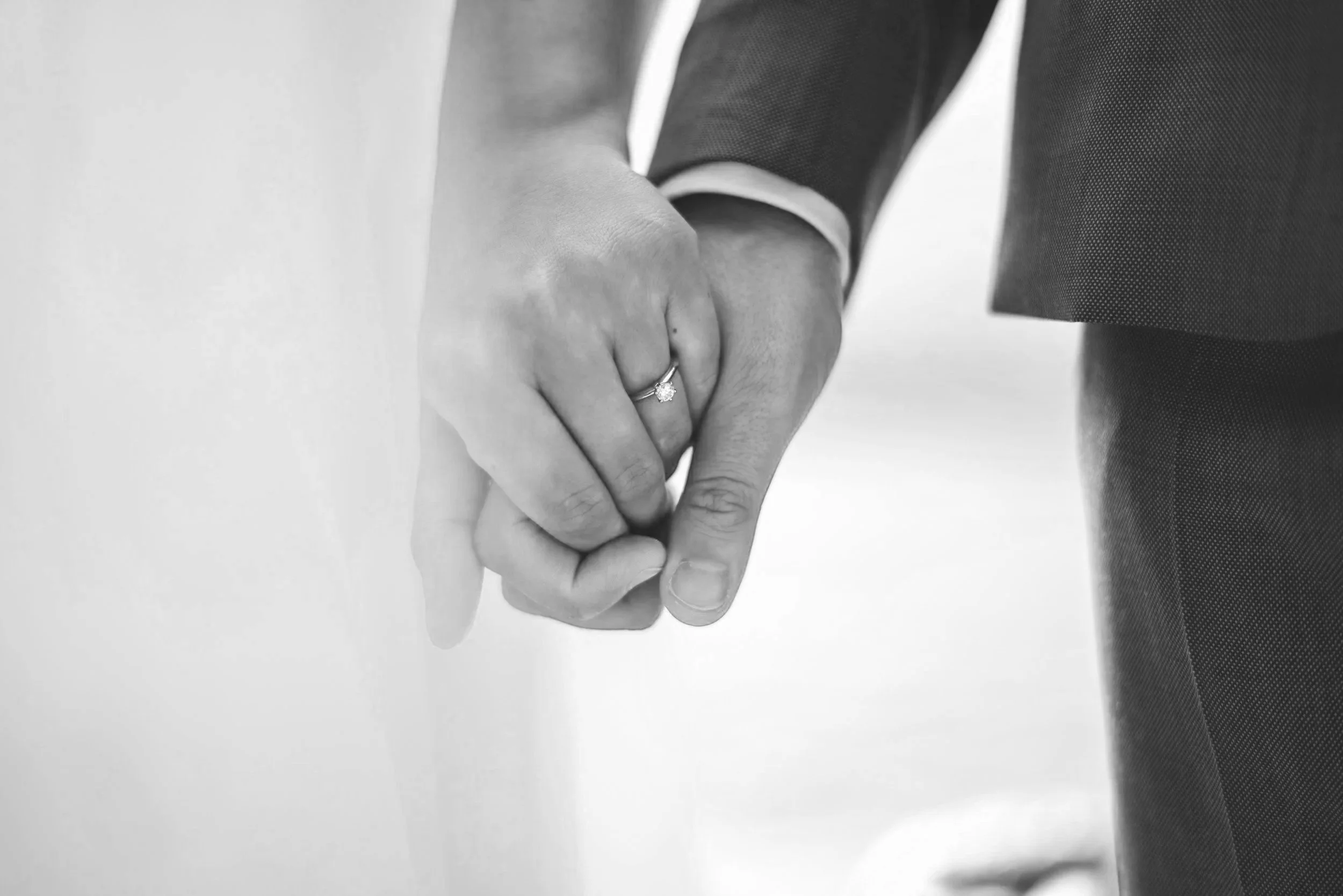 Close-up of a couple holding hands, with the woman wearing an engagement ring with a large diamond, in black and white.