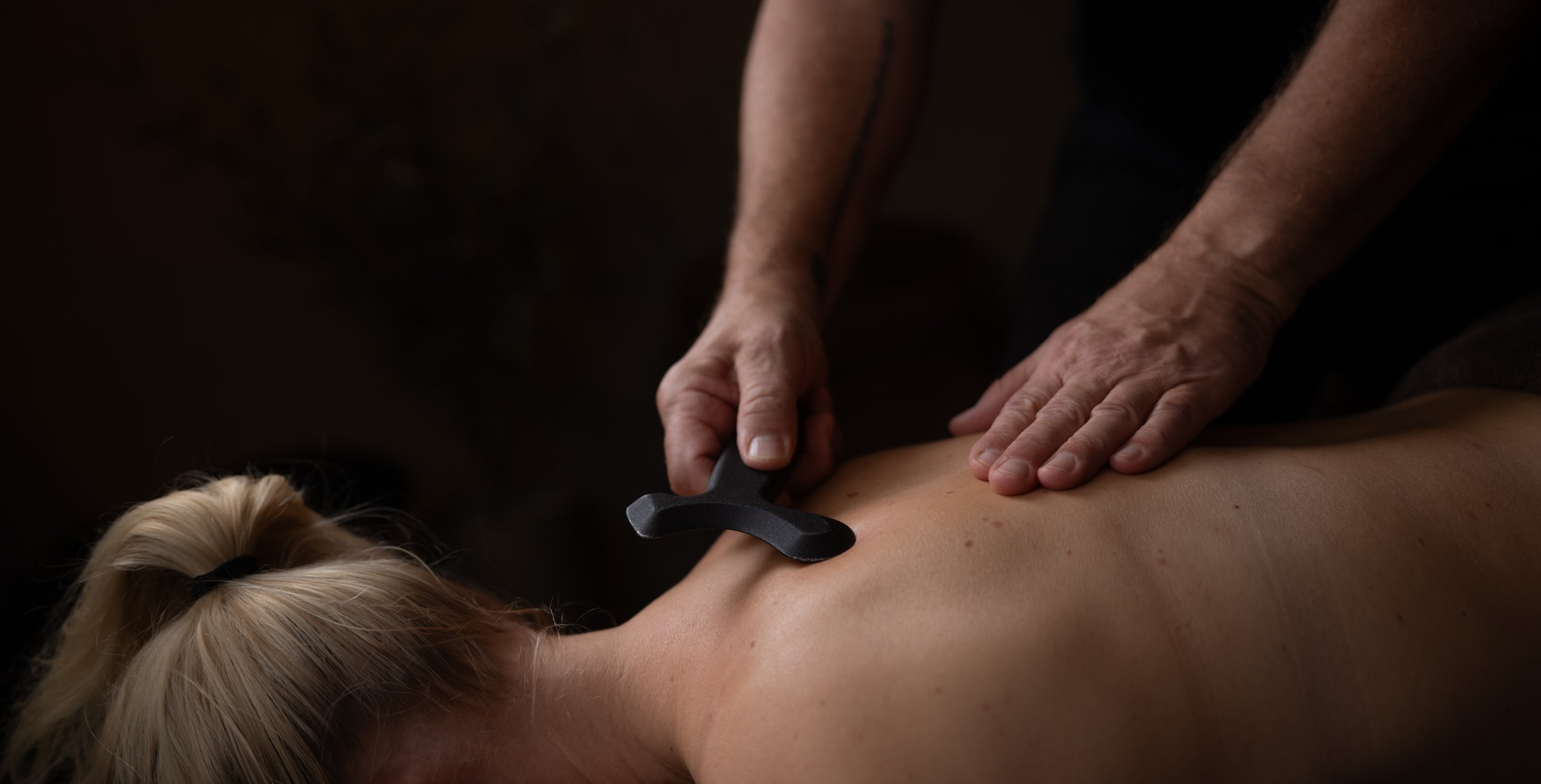 En person får en ryggmassage med en massagepinne av en massa terapeut i ett rum.