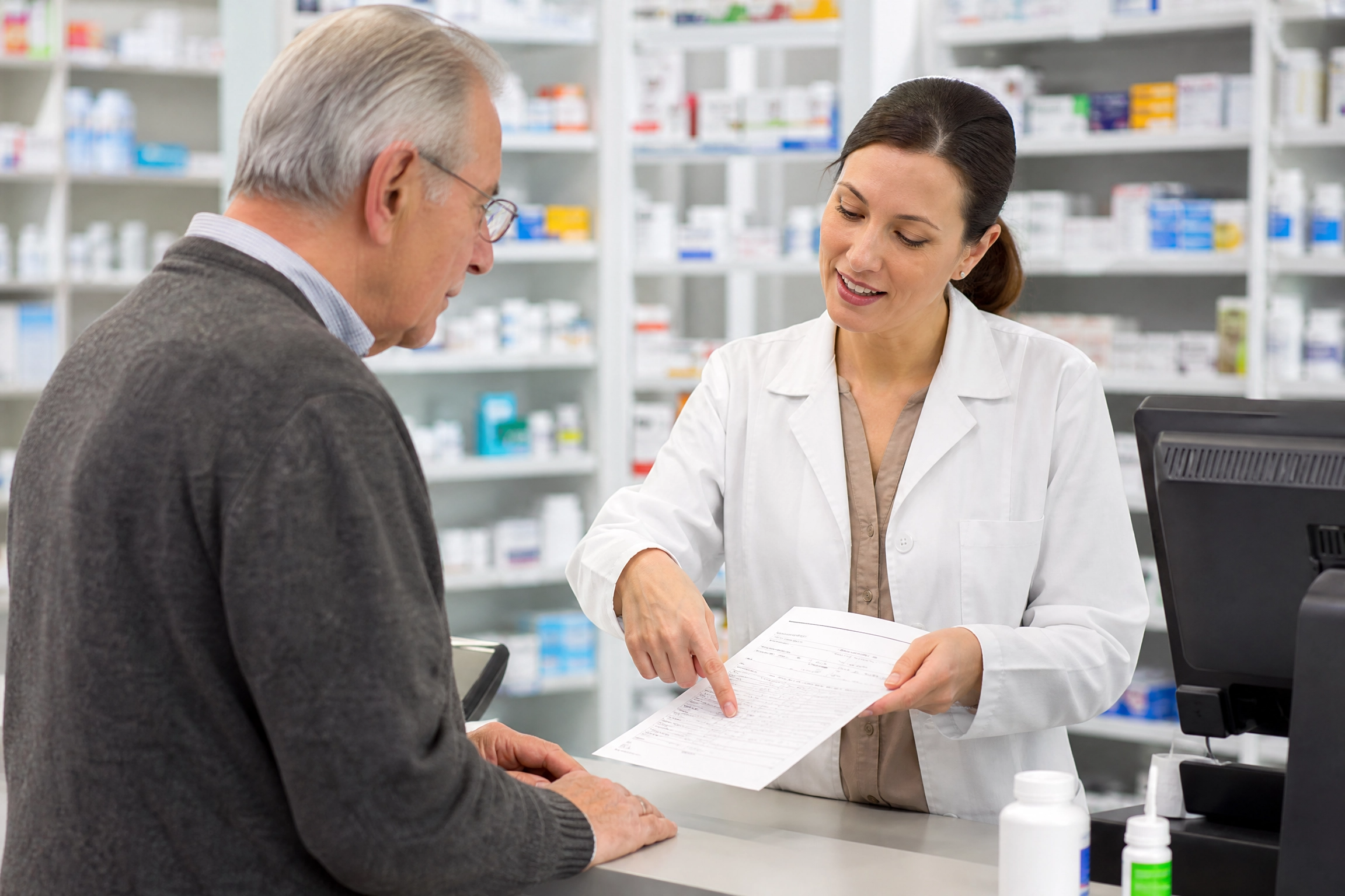 Senior man at pharmacy counter reviewing Medicare Part D prescription drug plan changes with pharmacist
