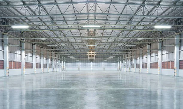 Empty large indoor warehouse or industrial space with high ceilings and metal framework.
