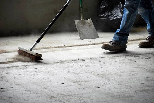 Person sweeping a concrete floor with a broom and shoveling dust with a shovel.