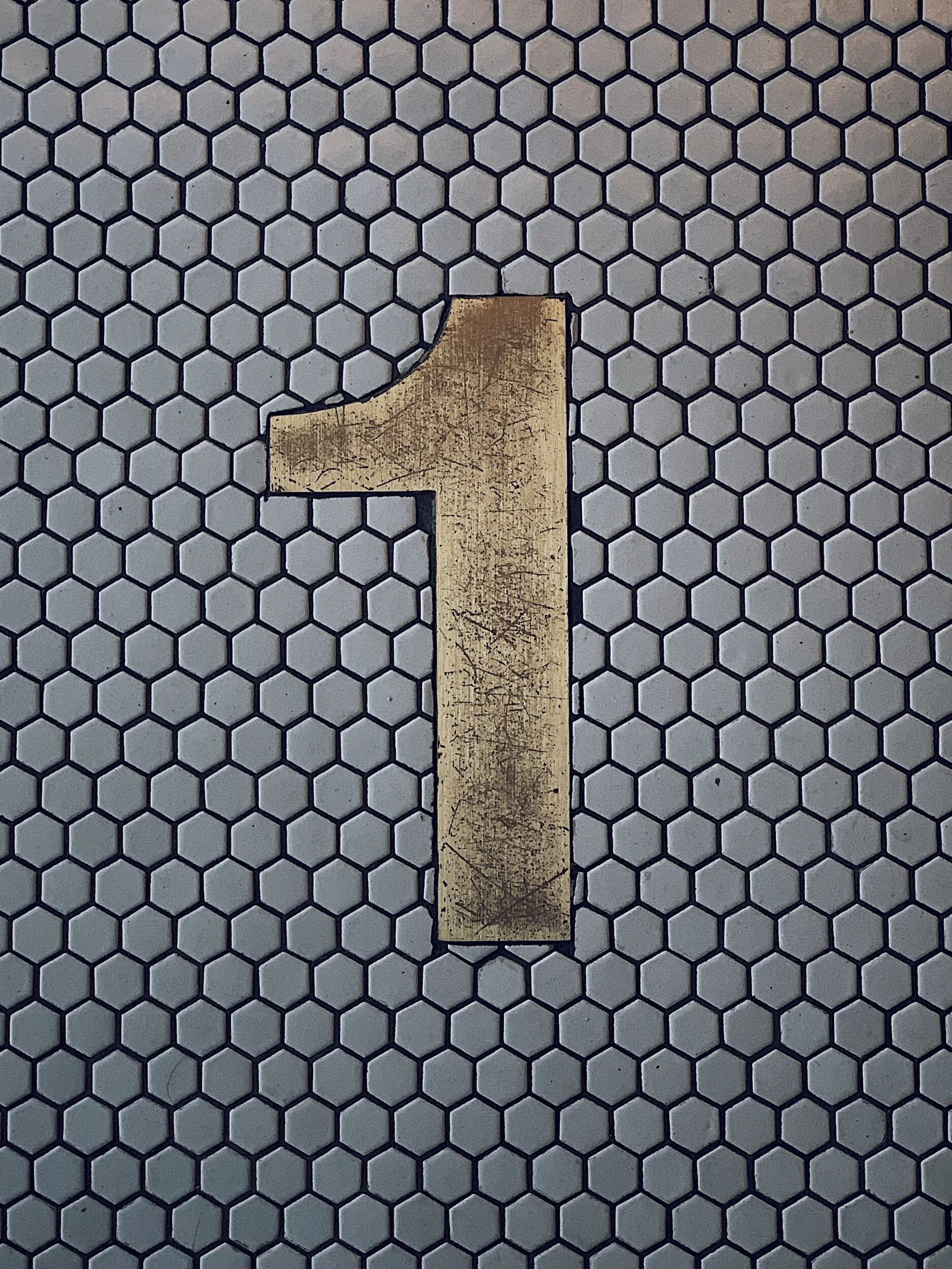 A large, metallic number 1 on a white hexagonal tile floor.