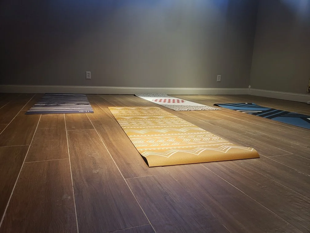 Four yoga mats laid out on a wooden floor in a cozy yoga studio with gray walls and baseboards.
