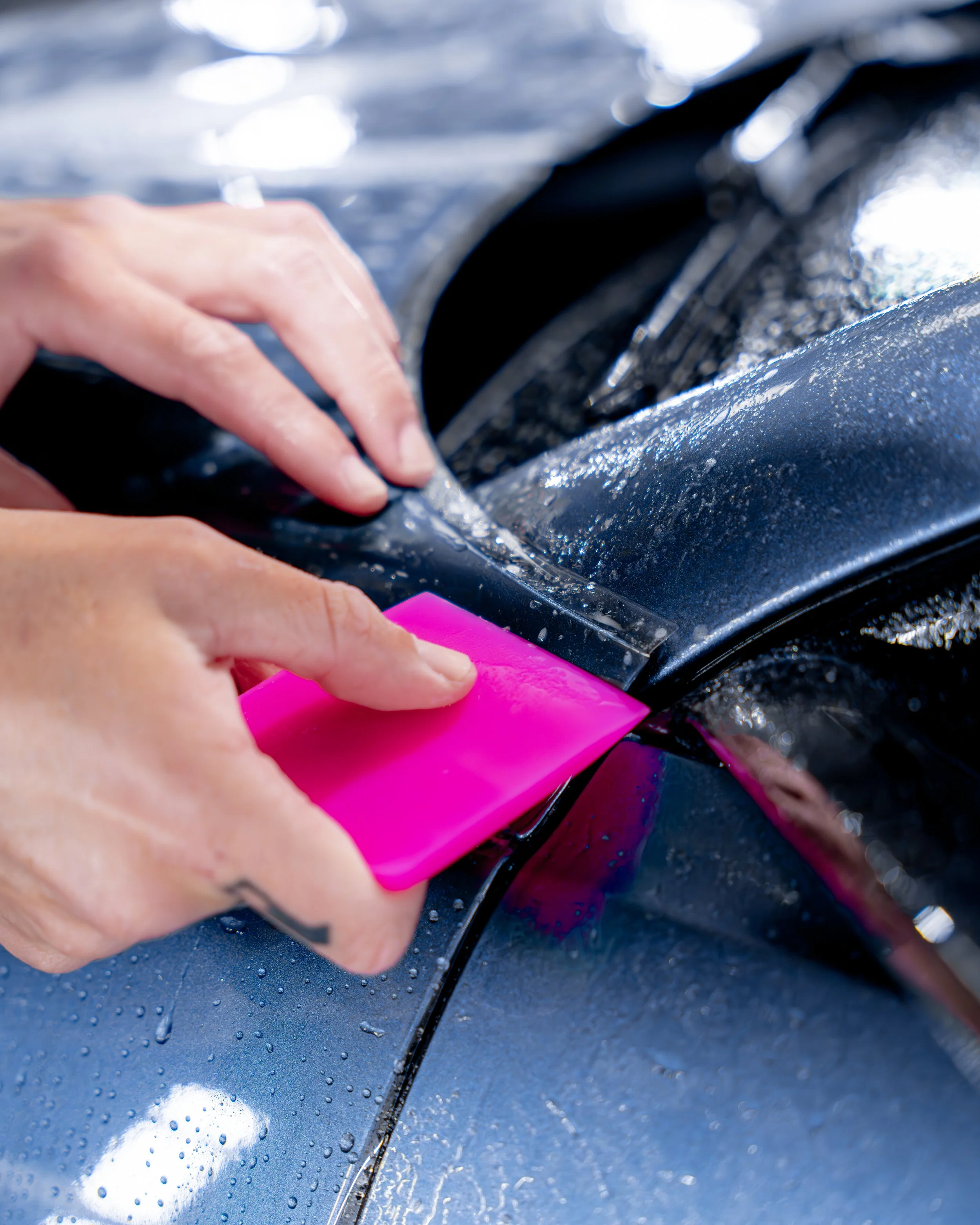 Person applying ppf to a car's fender with a pink applicator pad.