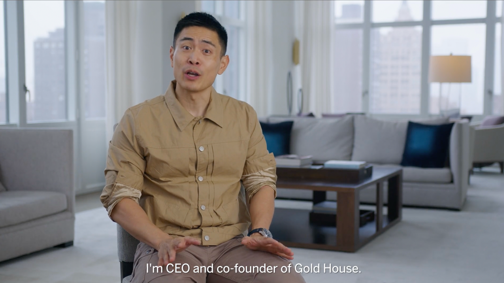 A man seated for an interview in a bright living room, with subtitles identifying him as CEO and co-founder of Gold House