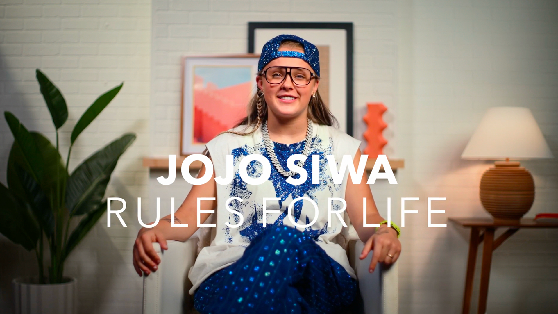 JoJo Siwa smiles while seated in a chair during an interview, with the text “JoJo Siwa Rules for Life” overlaid on screen