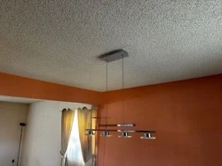 State-certified asbestos inspector sampling a textured popcorn ceiling in a hallway during a residential lighting fixture upgrade.
